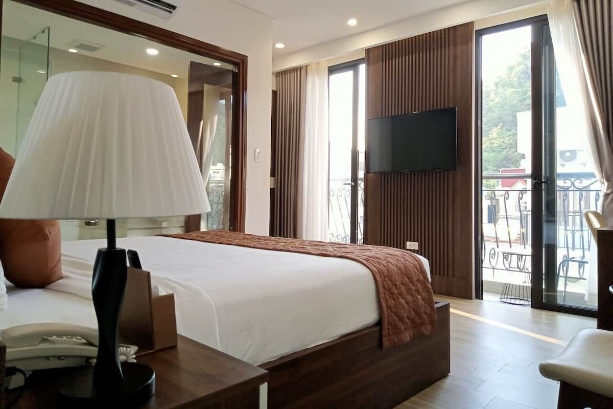 A hotel room with a large bed, a desk with a telephone, a lamp, and a flat-screen TV.