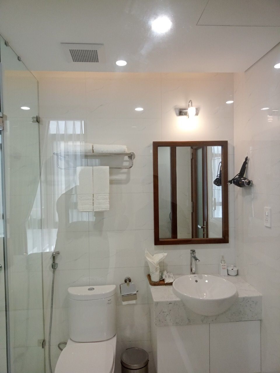 A modern bathroom with a glass shower enclosure, a white toilet, a sink with a marble countertop, and a mirror with a wooden frame.