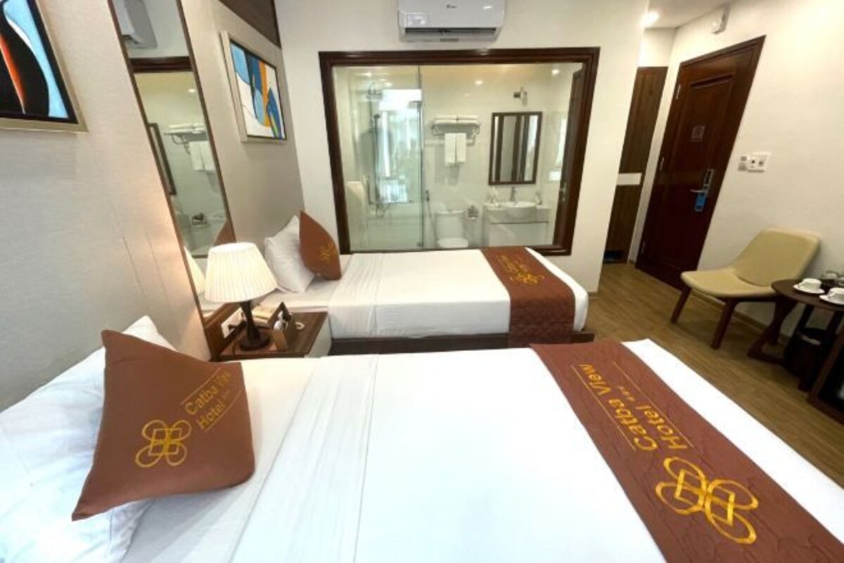 Habitación de hotel con dos camas, una zona de estar y un baño visible a través de una puerta de cristal.