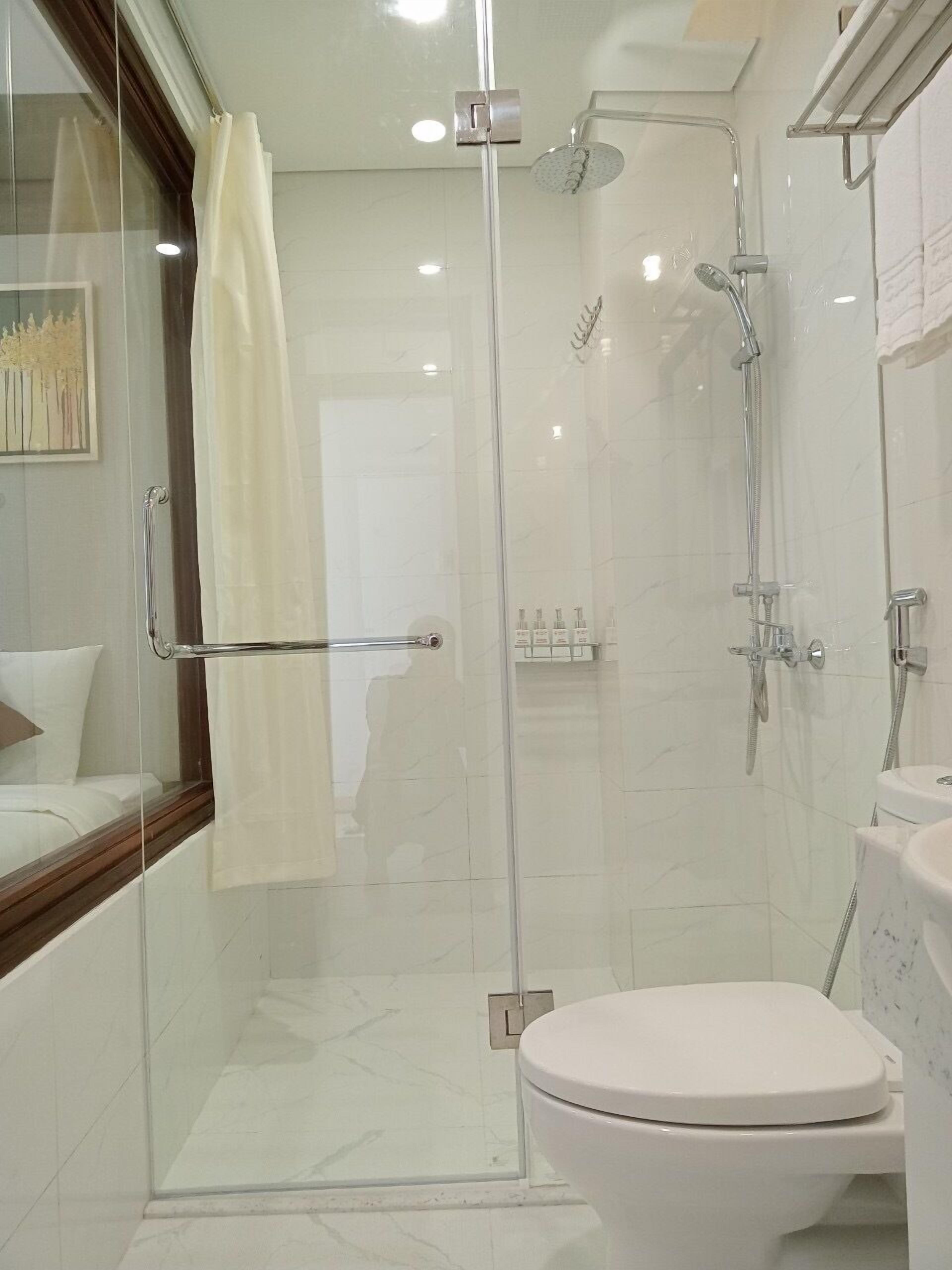 A modern bathroom with a glass-enclosed shower, a toilet, and a glass door leading to a bedroom.