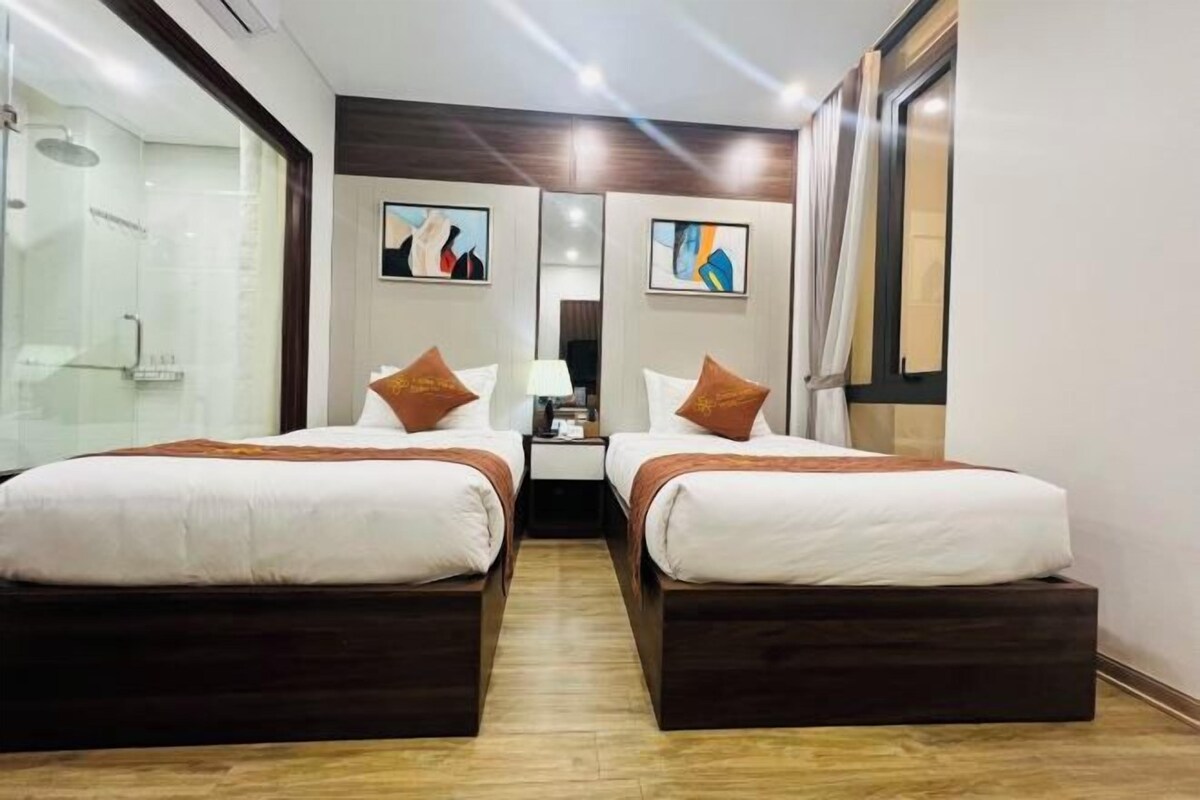 A hotel room with two beds, a shower area, and artwork on the walls.