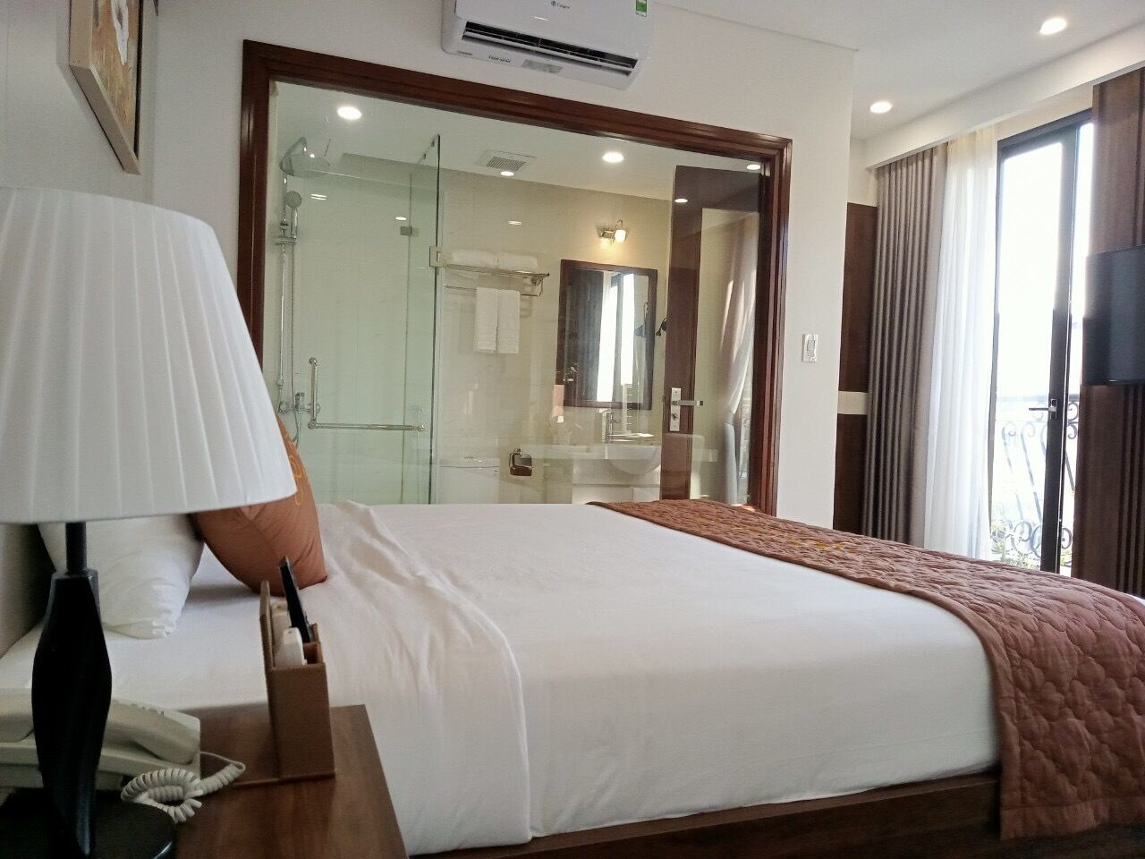A hotel room with a large bed, a bedside lamp, a mirror, and a view of the bathroom.