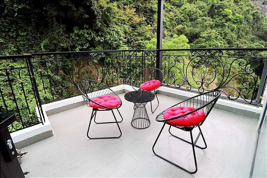A balcony with three chairs and a small table, surrounded by a wrought iron railing.