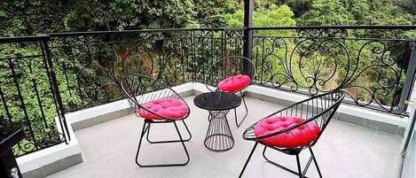 A balcony with three chairs and a small table, surrounded by a wrought iron railing.