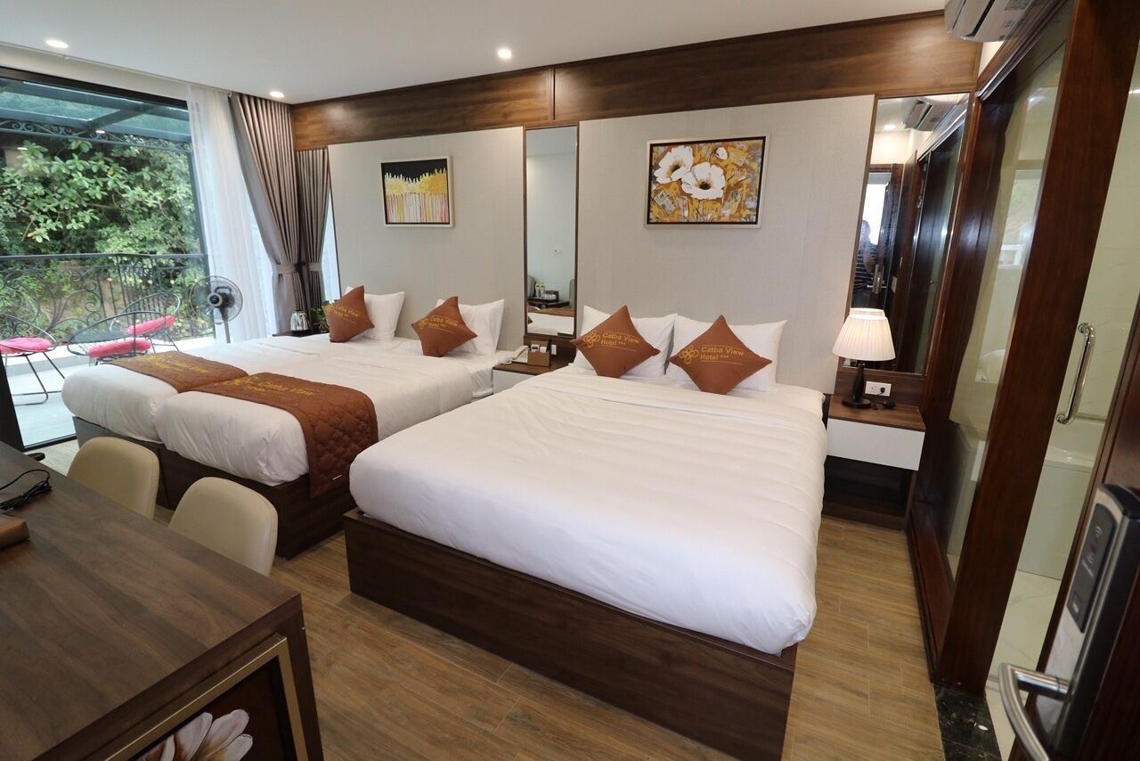 A hotel room with two beds, a wooden desk, a chair, a mirror, and a view of greenery outside.