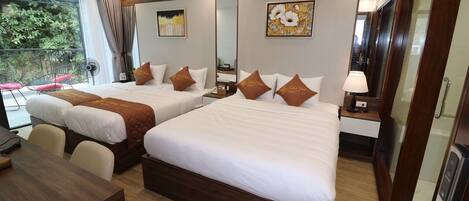 A hotel room with two beds, a wooden desk, a chair, a mirror, and a view of greenery outside.