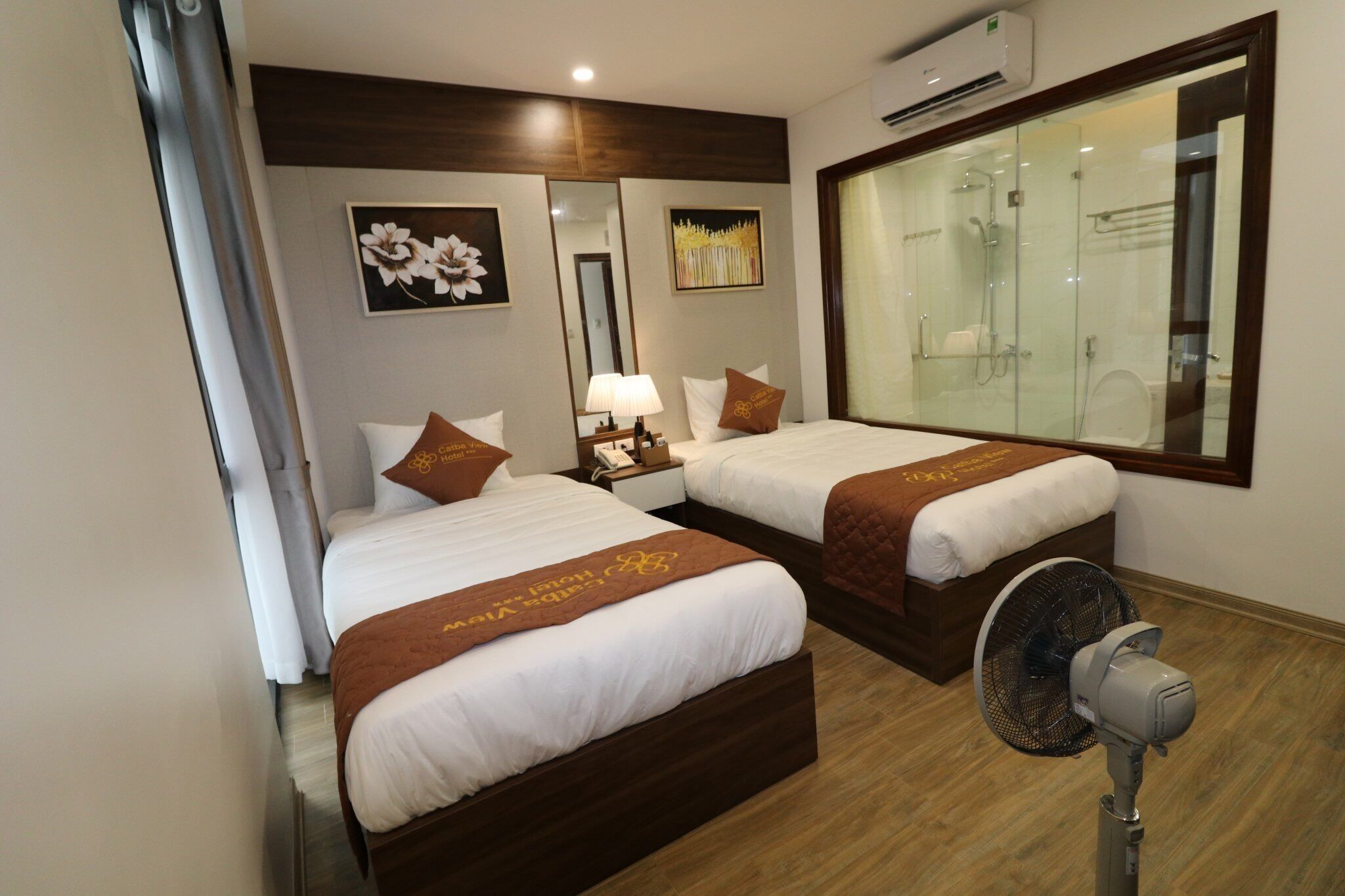 Une chambre d’hôtel avec deux lits, un grand miroir, un ventilateur et une vue sur la salle de bain.