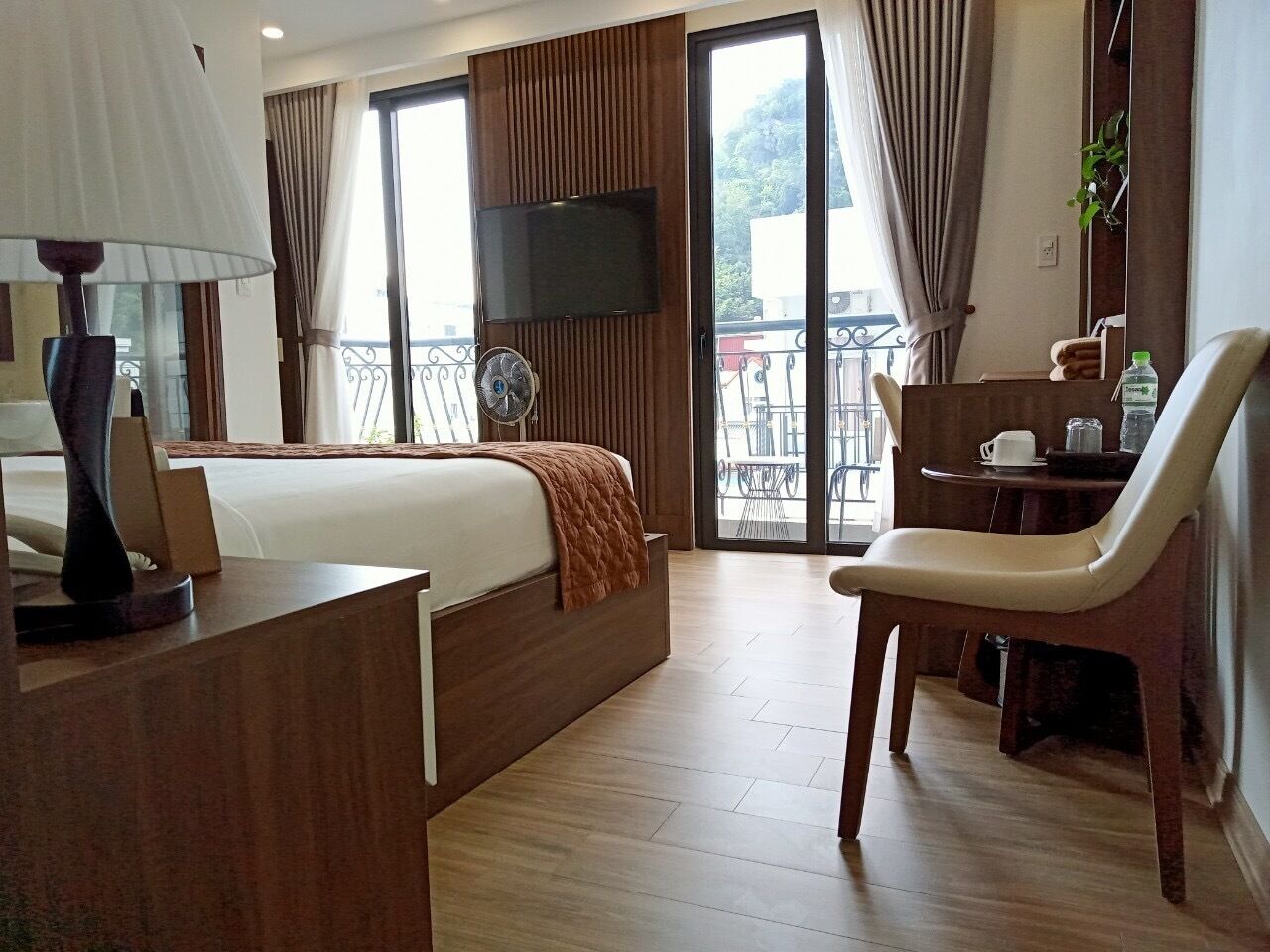 Habitación de hotel con cama, escritorio, silla, televisor y balcón con vistas.