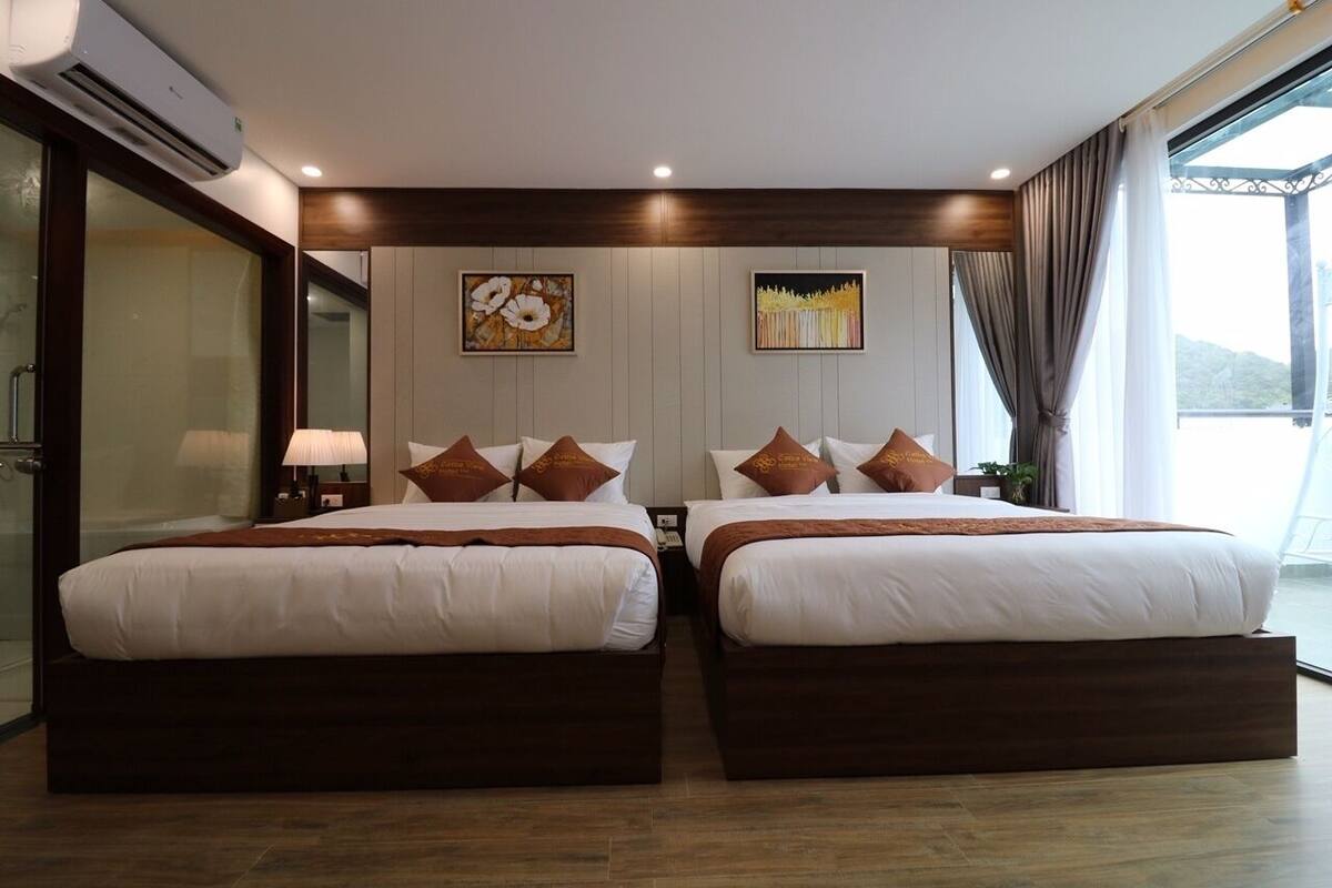 A hotel room with two beds, a large window with curtains, and artwork on the wall.
