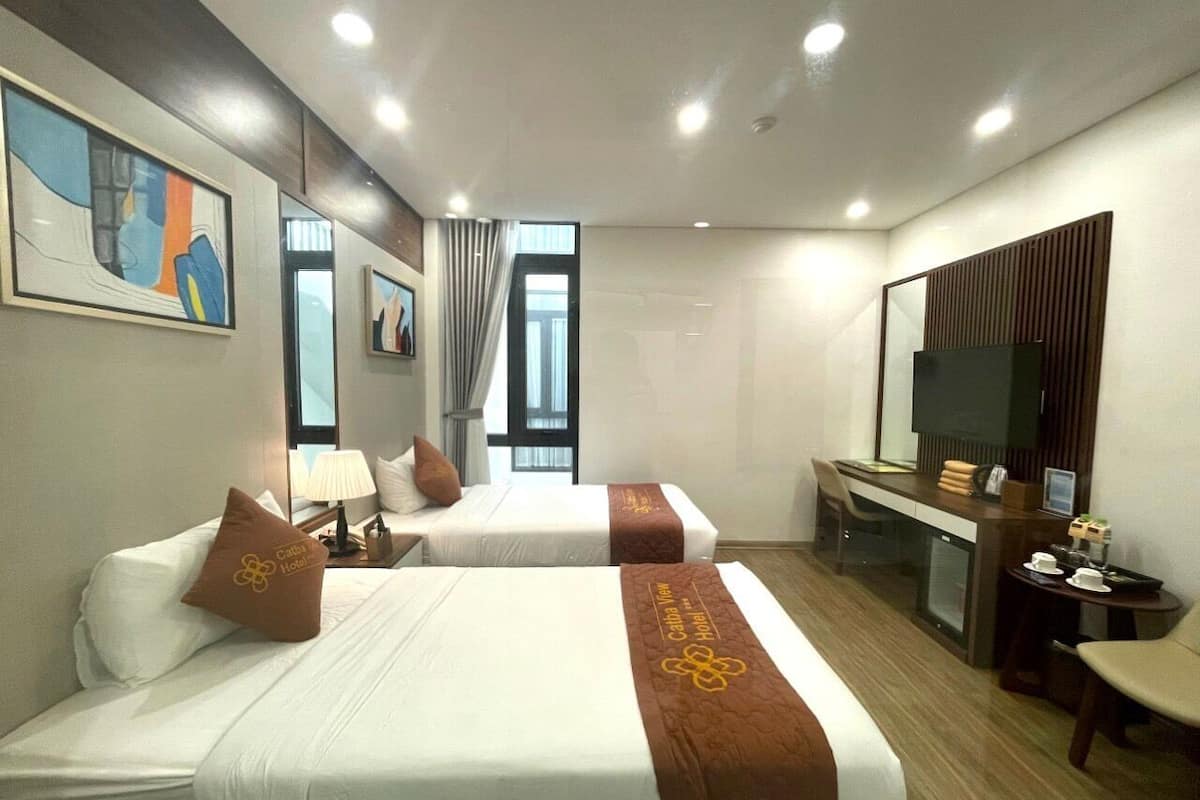 A hotel room with two beds, a desk, a TV, and a window with curtains.