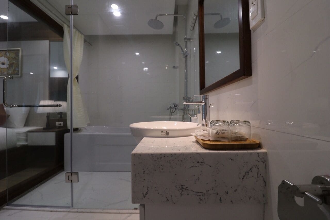Een moderne badkamer met een douchecabine van glas, een witte wastafel en een marmeren aanrecht.