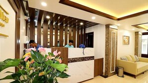 A hotel reception area with a marble reception desk, a potted plant, a sofa, and a trash bin. - Catba View Hotel (Hai Phong)