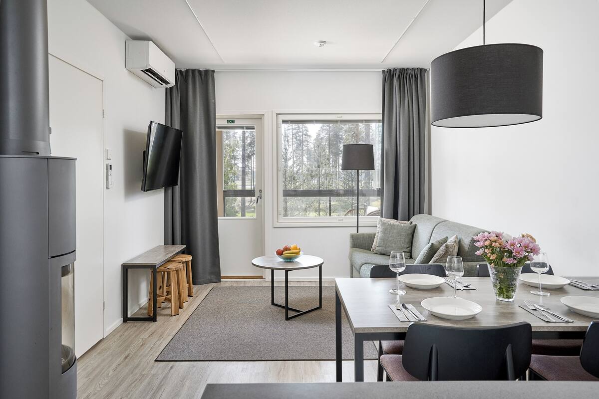 Een moderne keuken met een ingebouwde kookplaat, een eethoek met een tafel gedekt voor vier personen, en een groot raam met gordijnen.