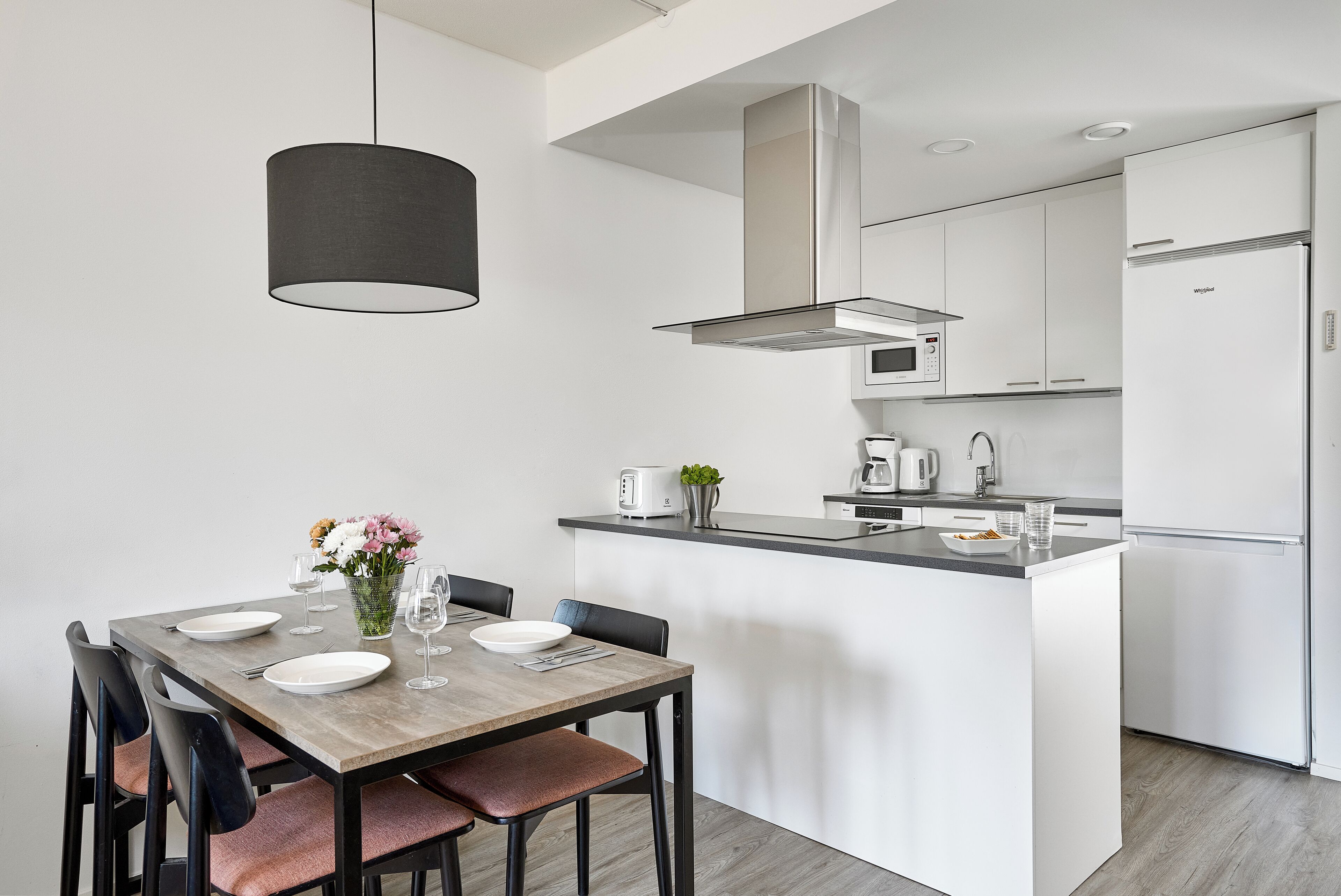 Une cuisine moderne avec des meubles blancs, un îlot central et un coin repas avec une table dressée pour deux personnes.