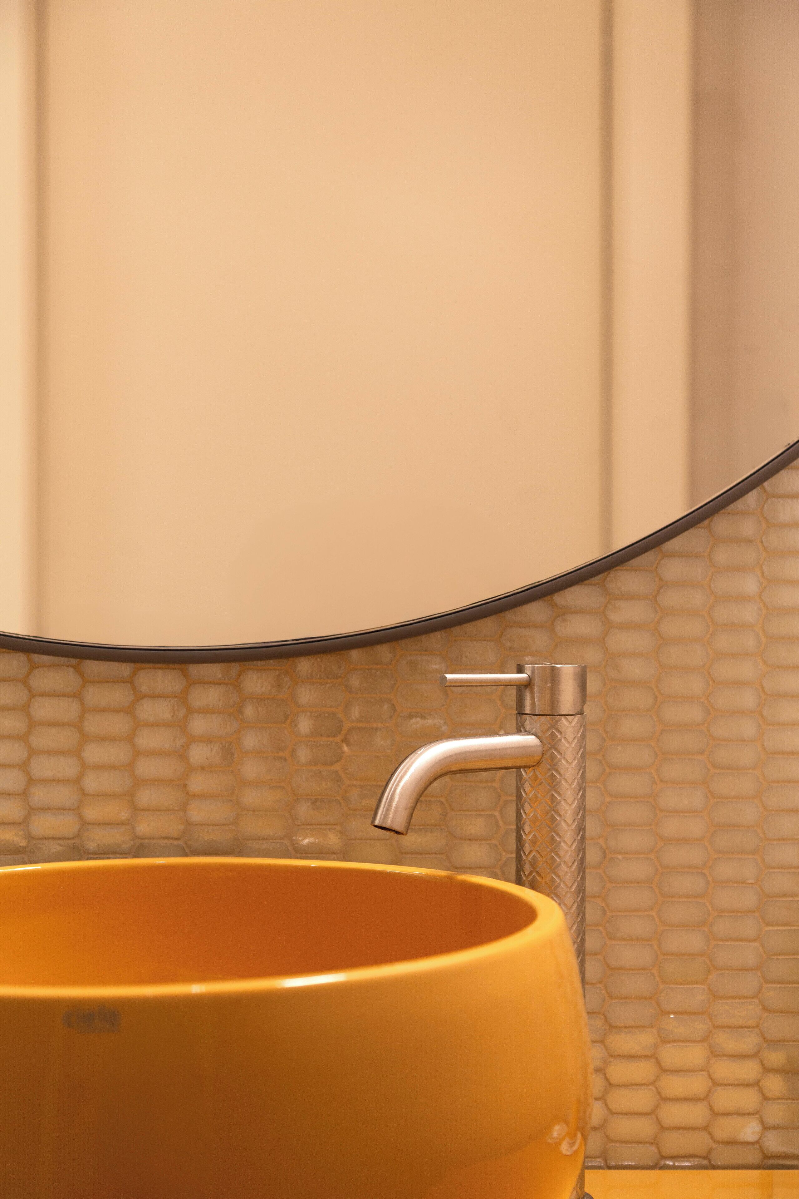 A bathroom with a yellow sink, a modern faucet, and a tiled wall.