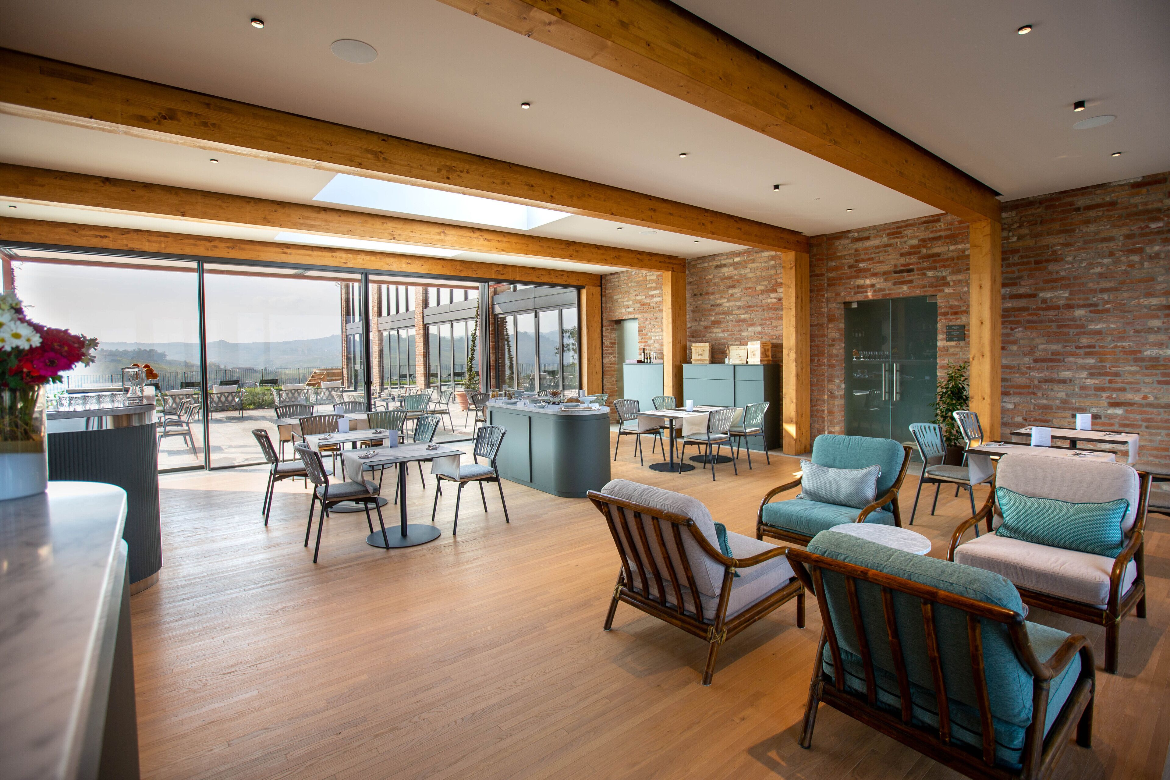 Un espacio interior amplio con pisos de madera, ventanas grandes y una variedad de opciones de asiento, incluyendo sofás y sillones.