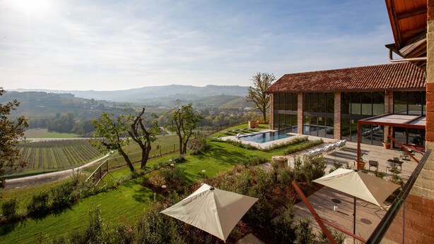 Zona de piscina con vistas al campo, mobiliario exterior y una sombrilla grande.