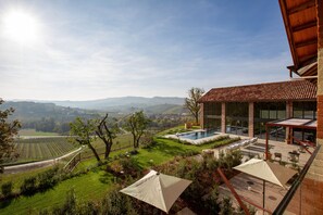 A pool area with a view of the countryside, outdoor seating, and a large umbrella. - Villaggio Narrante - Cascina Galarej (Serralunga d'Alba)