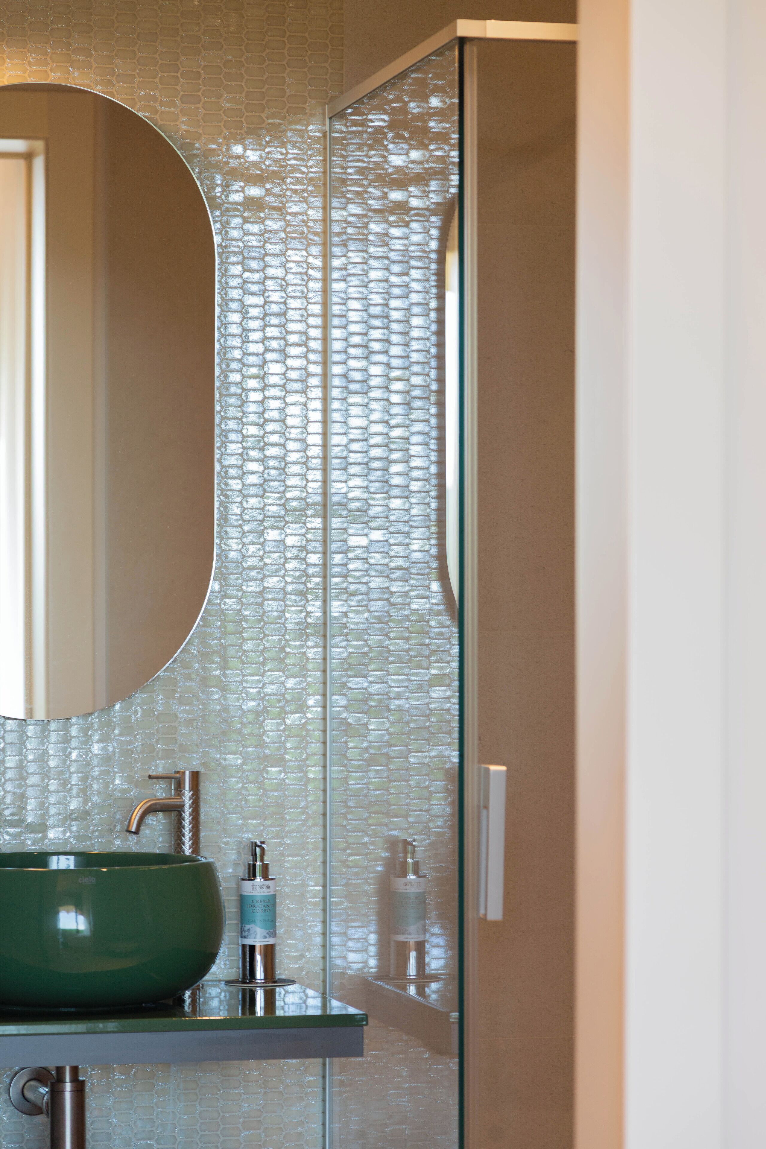 A bathroom with a green sink, a mirror, and a glass partition with a textured pattern.
