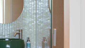 A bathroom with a green sink, a mirror, and a glass partition with a textured pattern.