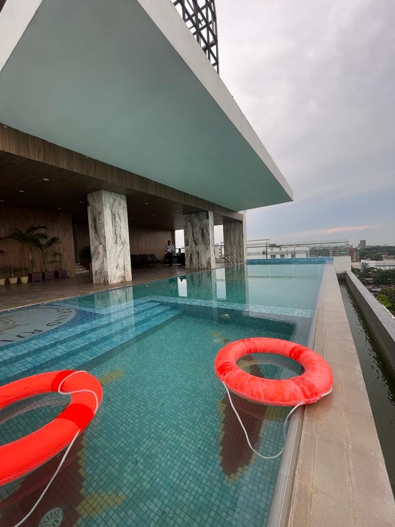 An indoor swimming pool with two red floating rings, a marble-tiled floor, and a view of the cityscape in the background.