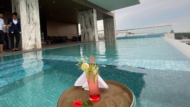 A pool area with a drink on a tray, marble columns, and a view of the sky. - Grand River View Hotel (Rajshahi)