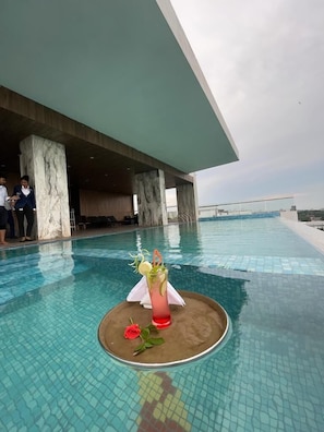Una piscina interior moderna con vista despejada al cielo, columnas de mármol y un área de descanso con gente.