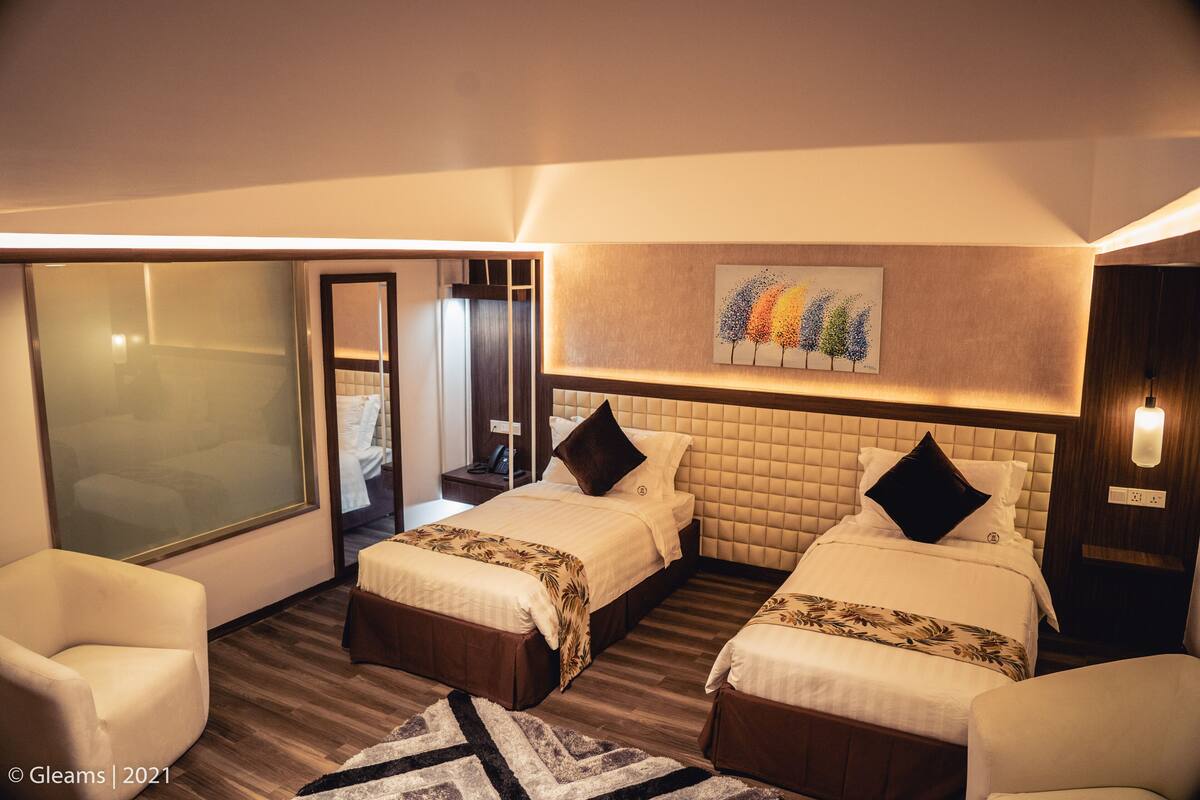 A hotel room with two beds, a large window, a painting on the wall, and a wooden floor.