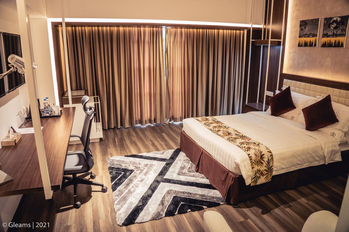 A hotel room with a bed, desk, chair, and curtains.