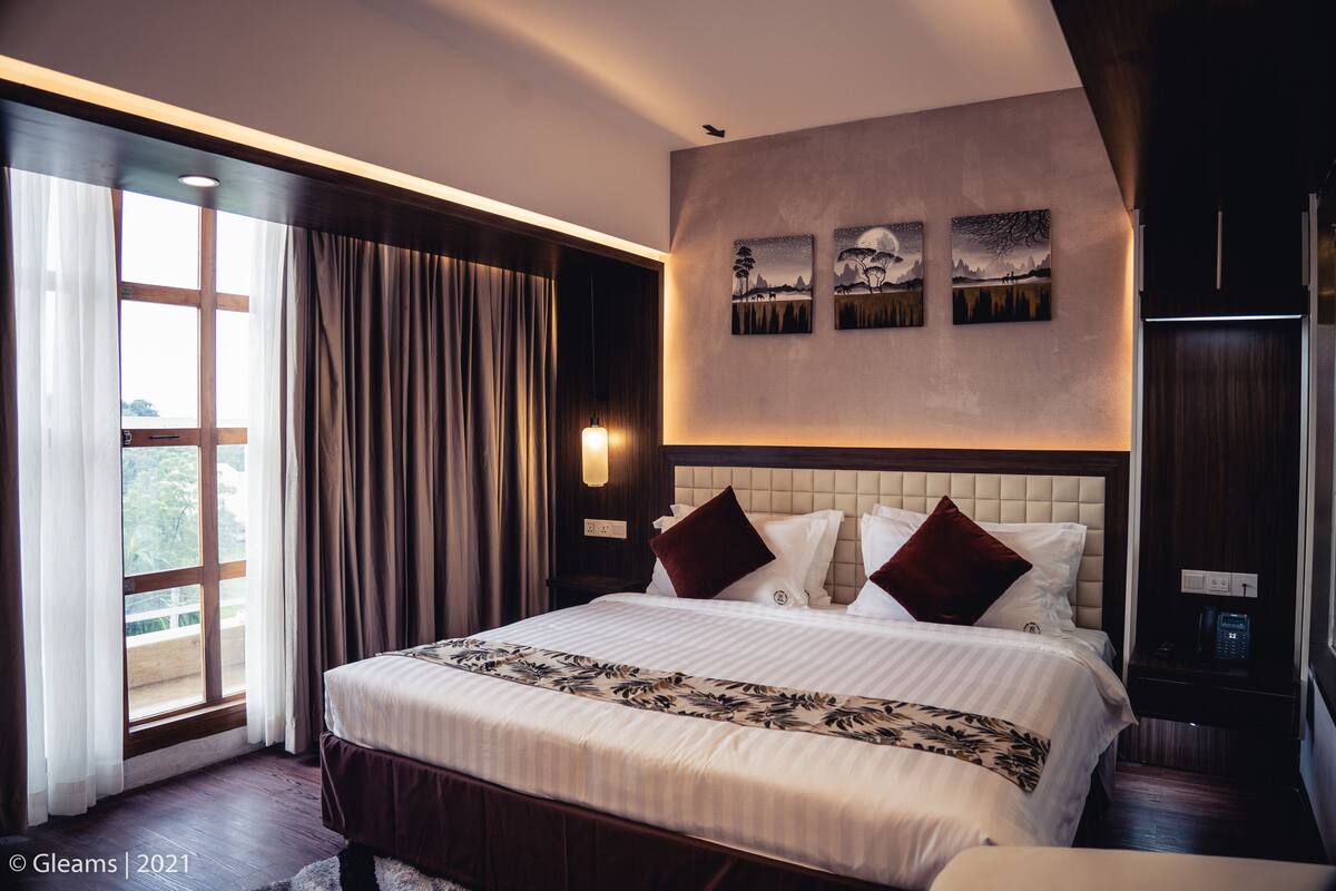 A hotel room with a large bed, a view through a window, and a wall-mounted artwork.