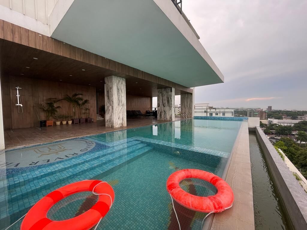A rooftop infinity pool with red floating rings, a wooden deck, and a city view.