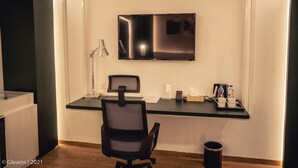 A modern hotel room with a flat-screen TV mounted on the wall, a desk with a chair, and a small trash bin. - Grand River View Hotel (Rajshahi)
