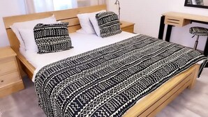 Una cama con una colcha estampada y almohadas, un cabecero de madera y una mesita de noche con una lámpara.