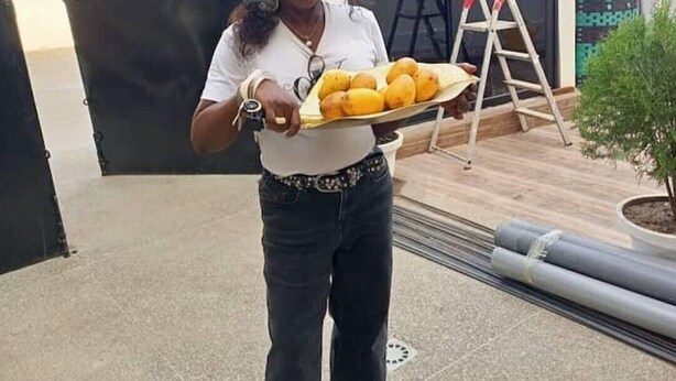 Una persona sosteniendo una bandeja con limones, frente a un edificio moderno con una puerta negra y una cerca de metal.