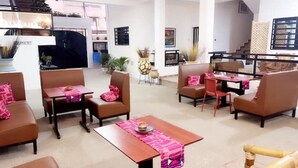 Un amplio salón con sofás y sillones de cuero marrón, una mesa de centro de madera y una mesa de comedor con manteles individuales rosas.