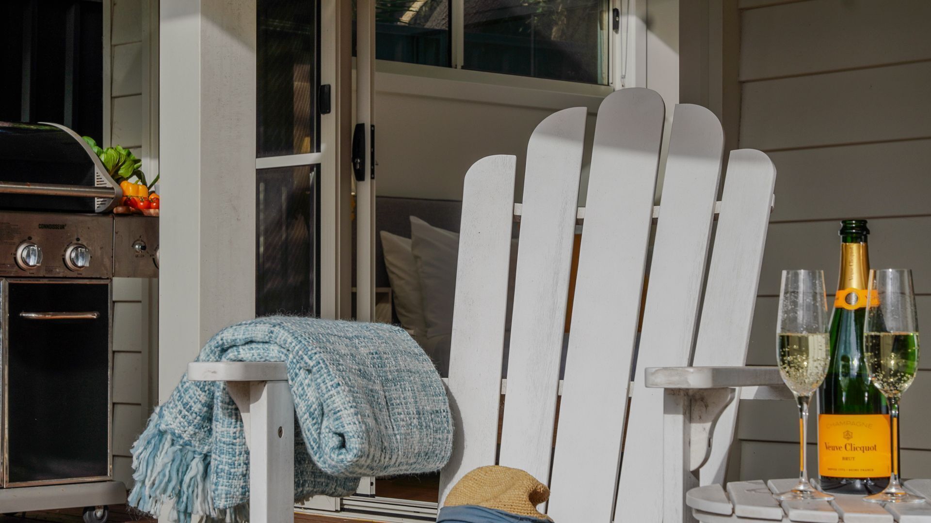 A white Adirondack chair with a blue throw blanket and a bottle of Veuve Clicquot champagne on a table.