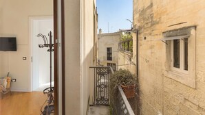 Un stretto vicolo con pavimento in legno, una porta bianca e un piccolo balcone con ringhiera in metallo.