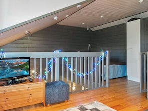 A room with a wooden floor, a television on a wooden stand, a grey bench, and a railing decorated with lights. - Kelkka 2 by Interhome (Salla)