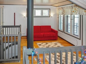 A room with a red sofa, a checkered rug, and a window with blinds.