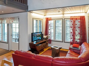 A living room with a red leather sofa, a wooden entertainment unit with a TV, and large windows with curtains. - Kelkka 2 by Interhome (Salla)