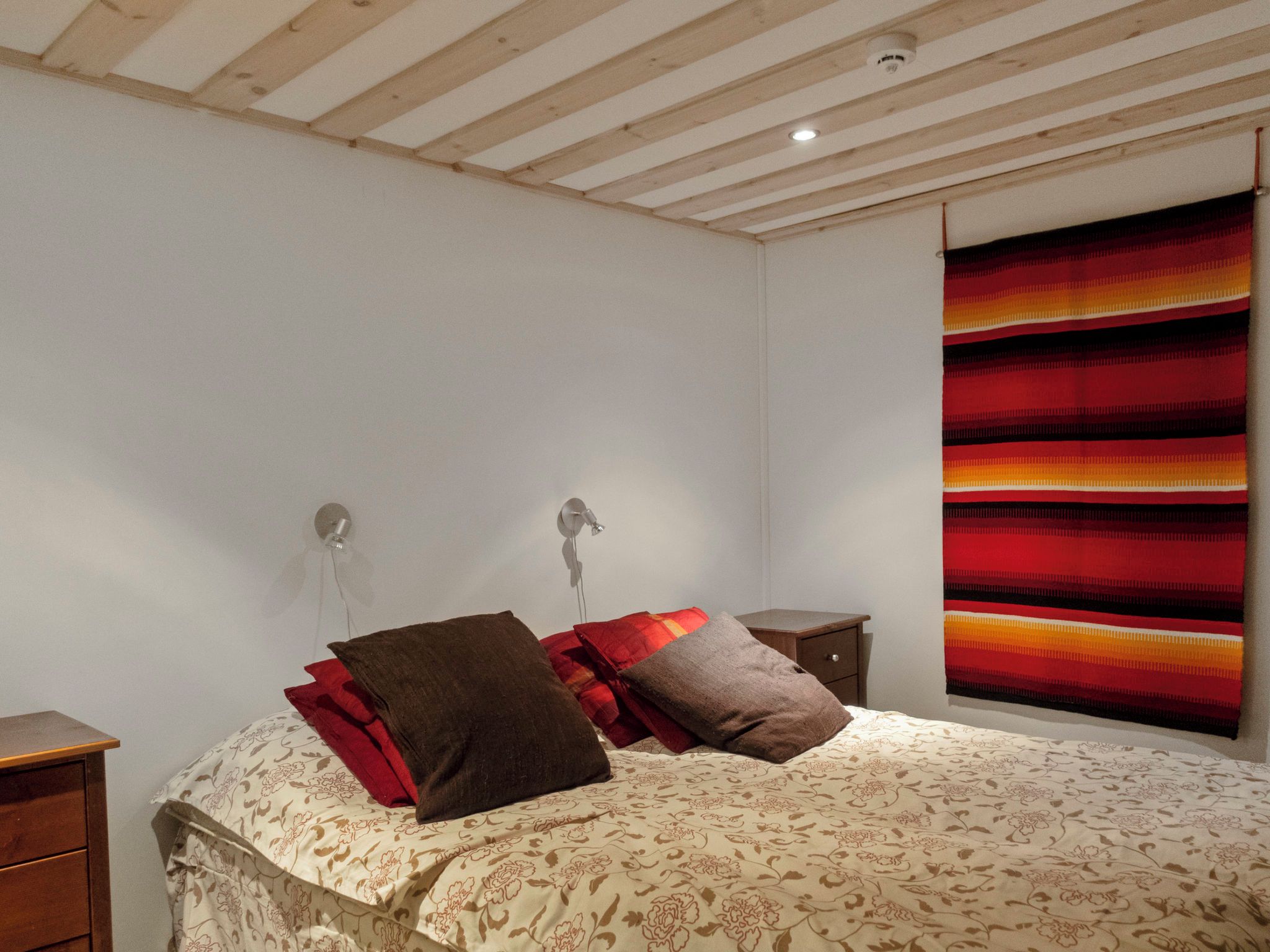 Ein Schlafzimmer mit einem Bett, zwei Nachttischen, einer Wandlampe und einem farbenfrohen Vorhang.
