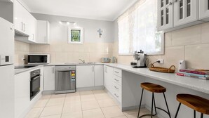 Una cucina moderna con mobili bianchi, lavastoviglie in acciaio inossidabile, microonde, macchina del caffè e una finestra con tende in pizzo.