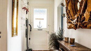 A hallway with wooden flooring, a white door, a vacuum cleaner, a decorative mirror, and a rustic wall piece. - Vacation home with 80 sqm - on Ballumweg on Sylt (Sylt)