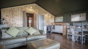Una sala de estar acogedora con sofá y reposapiés, paredes de madera, una cocina con refrigerador y un comedor con sillas y una mesa.