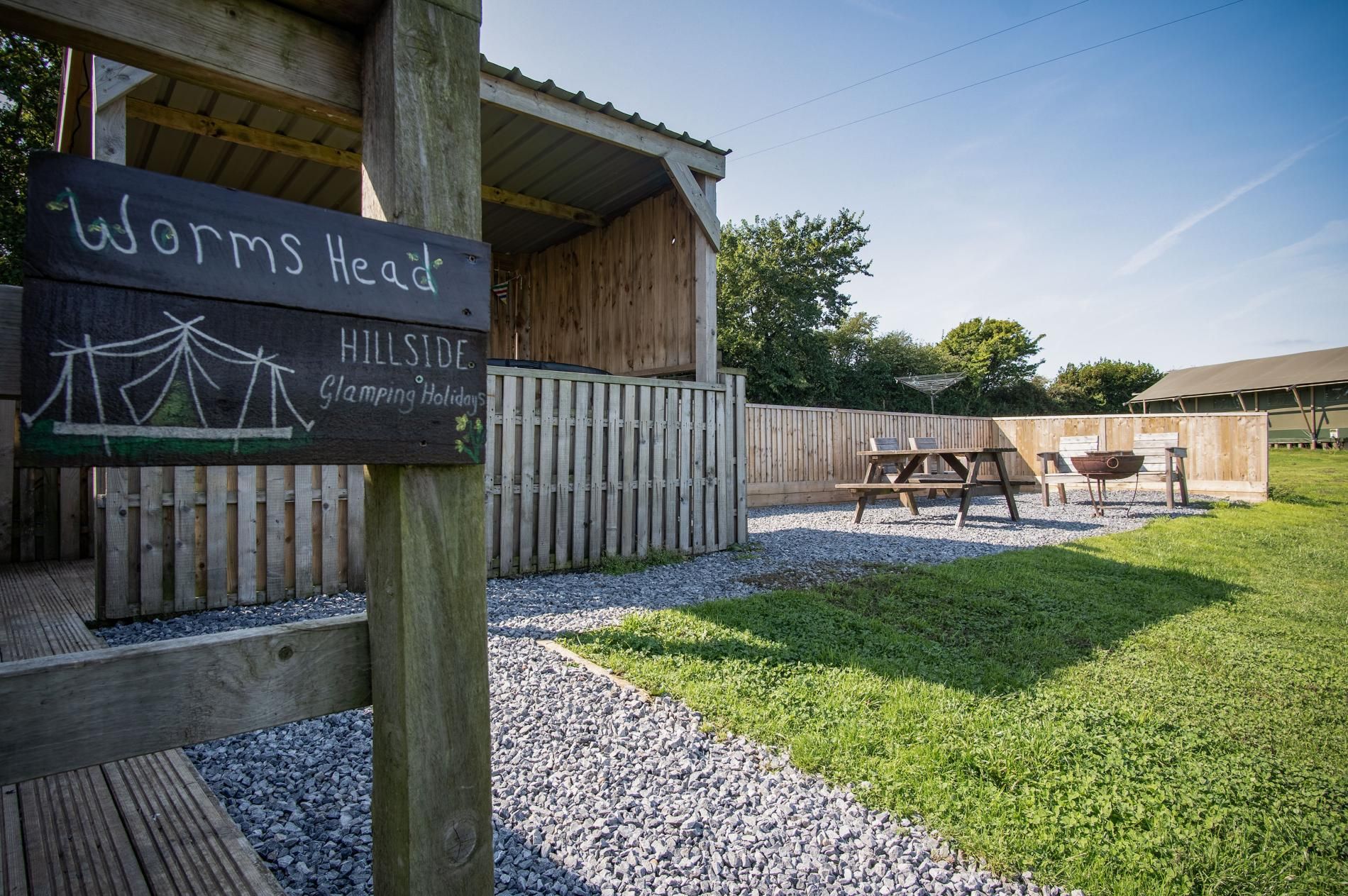 Un terrain de camping appelé « Worms Head », doté d’une structure en bois, de tables de pique-nique et d’une zone délimitée par une clôture.