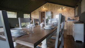 Un comedor con una mesa de madera dispuesta para cuatro personas, rodeada de sillas grises. Se ve un área de cocina al fondo, con armarios de madera y un fregadero.