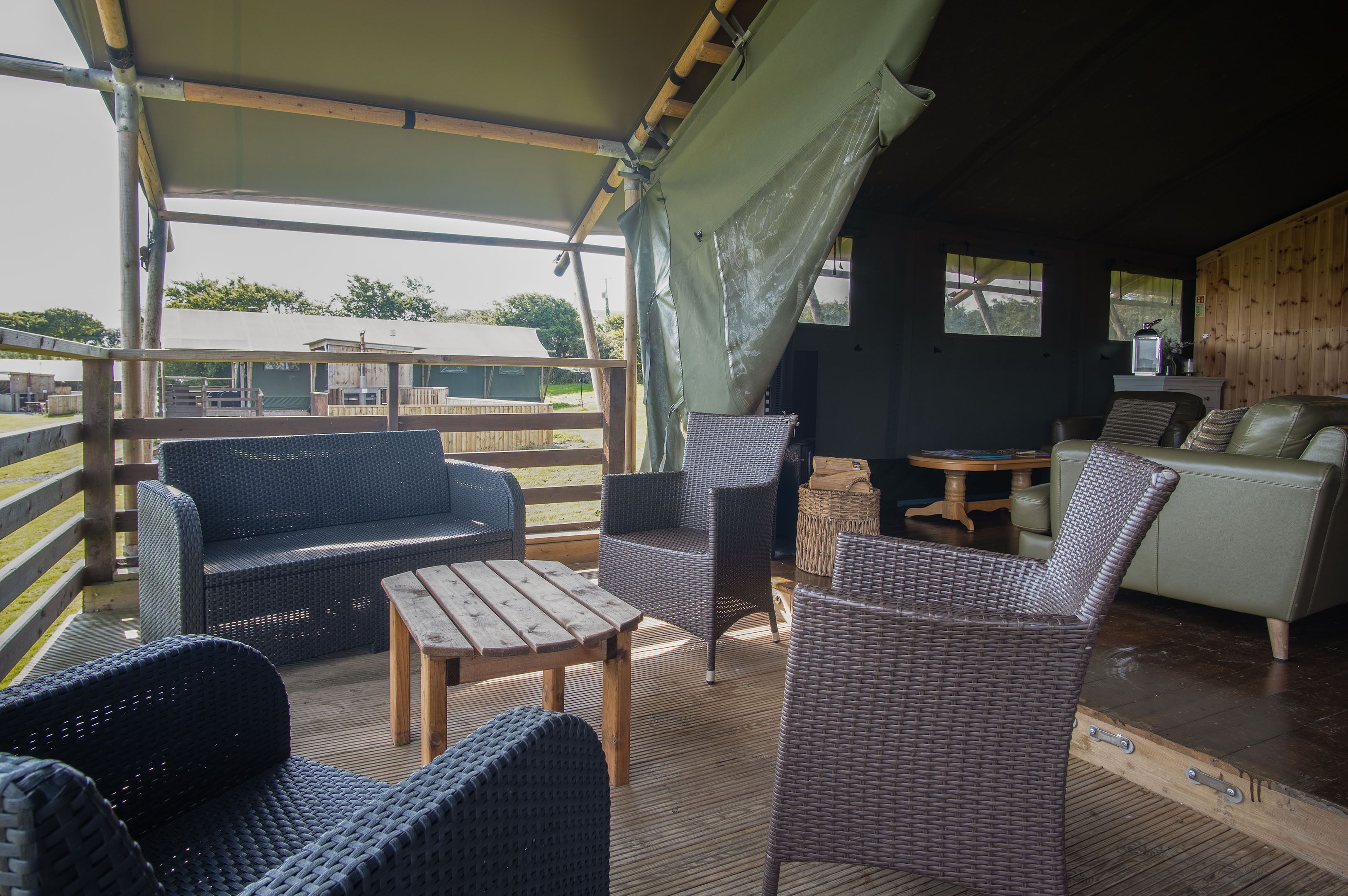 Un espace extérieur aménagé, abrité et doté de mobilier en osier, d’une table en bois et offrant une vue sur les environs.