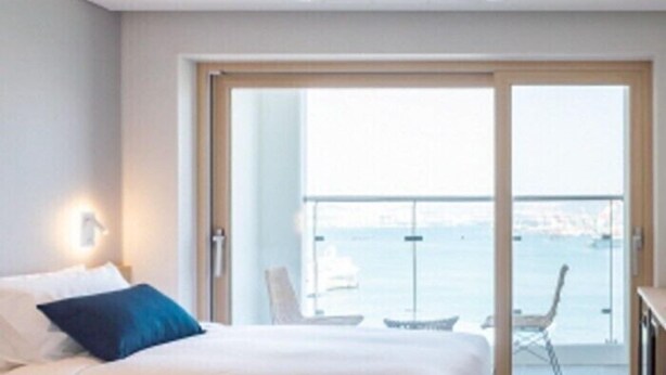 A hotel room with a bed, a nightstand, a chair, and a view of the sea through a sliding glass door. - Busan Connect Ocean Hotel (Busan)