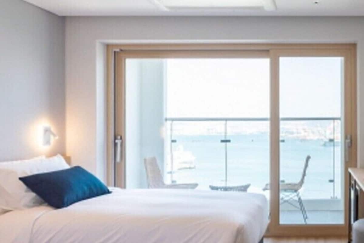 A hotel room with a bed, a nightstand, a chair, and a view of the sea through a sliding glass door.