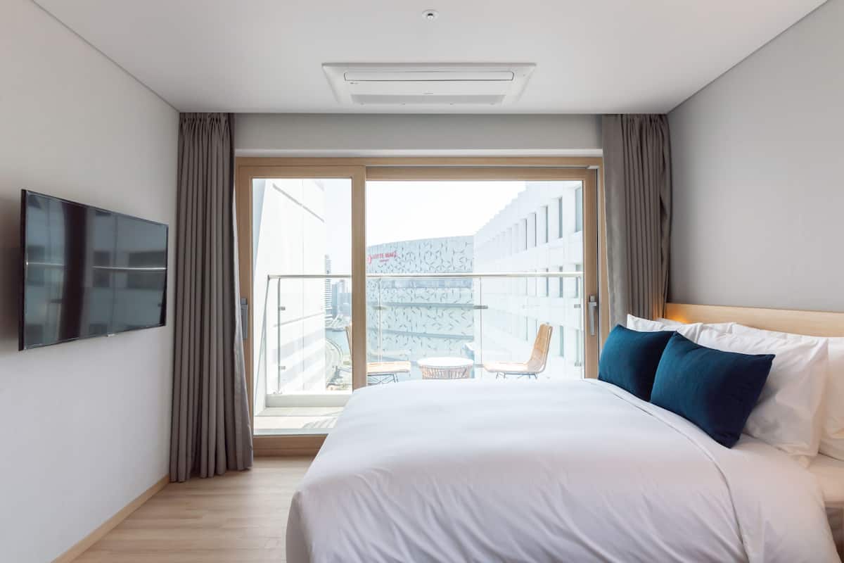 A hotel room with a large bed, a flat-screen TV, a balcony with a city view, and a modern design.